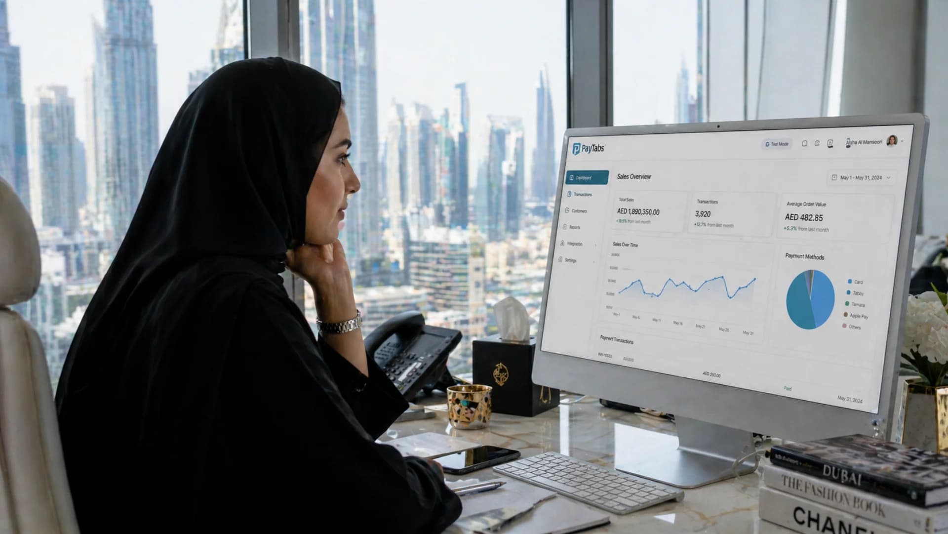 PayTabs integration in UAE — Emirati businesswoman reviewing PayTabs sales dashboard with Dubai skyline view